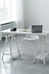 Work area with table and chair. A laptop notebook and headphones are on the table. Isolated on white background.