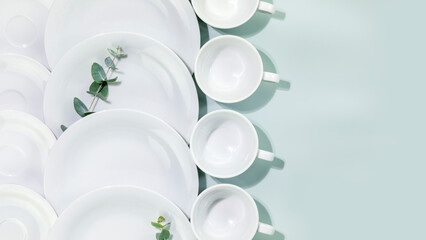 Clean, empty white dishes and cups with eucalyptus twigs on blue background with copy space. Eco friendly washing dishes and cleaning. Dishes, porcelain background. Flat lay