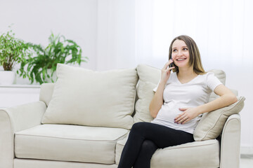 Obraz premium Pregnant woman talking over the phone on white sofa.