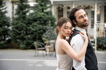 young woman in wedding dress hugging bearded groom in vest.