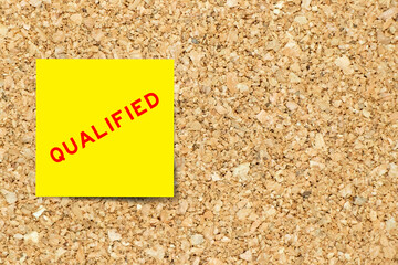 Yellow note paper with word qualified on cork board background with copy space