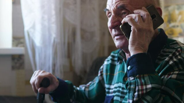 caucasian grandfather 70 years old sitting with a walking stick inside talking on the phone. call your parents, elderly people concept, real people