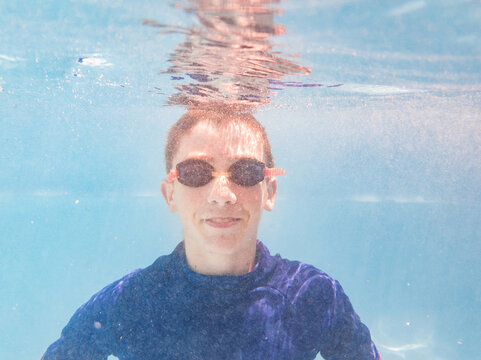 Teen boy swimming in pool underwater with goggles on