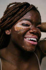 portrait of a beautiful African woman with vitiligo laughing as her hair is tied up so she can apply her exfoliating mask