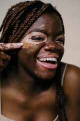 portrait of a beautiful african woman with vitiligo laughing while applying a natural sugar exfoliating mask