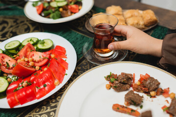 Cropped view of muslim boy holding traditional glass cup of tea near food at home.
