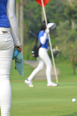 Blurry image of a female caddy walking while holding flag with foreground cropped shot of another caddy.