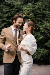 cheerful groom in suit and happy bride in wedding dress holding glasses of champagne.