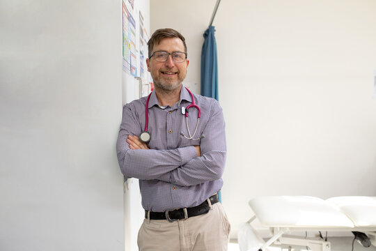 Male doctor with stethoscope around his neck standing while leaning on the wall in the clinic