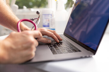 Close up shot of a laptop with a healthcare professional using it while holding a stethoscope