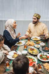 Smiling muslim parents talking near kids and iftar dinner at home.