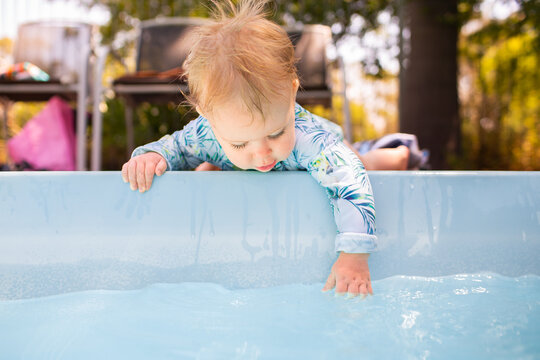 Young baby leaning over edge of inground swimming pool splashing in water – dangerous situation