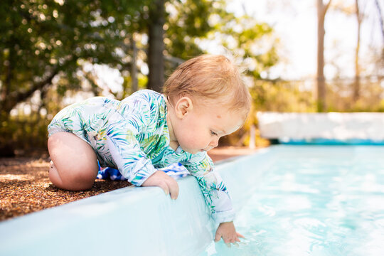 Young baby leaning over edge of inground swimming pool splashing in water – dangerous situation