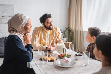 Muslim man holding prayer beads near family and ramadan breakfast at home.