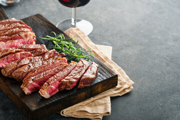 Steaks. Sliced grilled meat steak New York or Ribeye with spices rosemary and pepper on black marble board on old wooden background. Top view. Mock up.