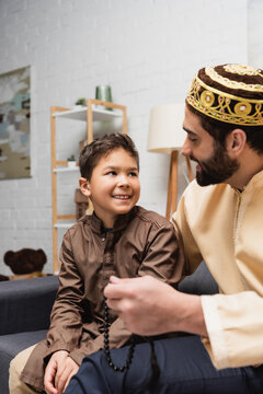 Smiling muslim boy looking at father with prayer beads at home.