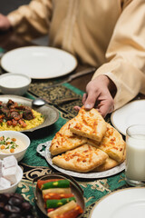 Cropped view of muslim man taking pita bread near food during ramadan dinner.