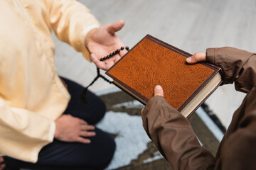 Cropped view of muslim boy holding koran near father with prayer beads at home.