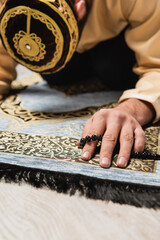 Blurred muslim man with prayer beads praying on carpet at home.