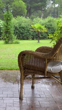 Relaxing scene of a garden with a lot of green being bathed by rain and a gentle breeze. All seen from a close-up where you can see an empty straw chair. 4K footage Vertical