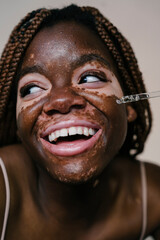 portrait of a pretty african woman with vitiligo applying an essence serum with a dropper while smiling