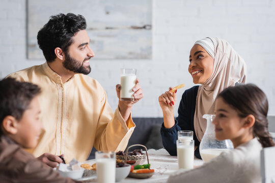 happy muslim parents looking at each other near blurred kids and suhur breakfast at home.