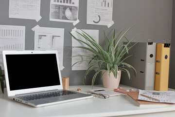 Fototapeta premium Workplace at home or in office with table, laptop with empty display, flower, paper folders, notes on wall.