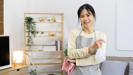 Asian housewife wearing apron holding rag and cleaning spray prepares for a big cleanup in the house, Housework, Daily routine, Big cleaning, Deep stain remover, Clean up on weekends.