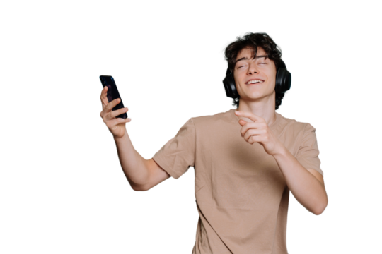 Handsome caucasian young guy listening music uses headphones holds phone eyes closed against transparent background. Joyful schoolboy dancing smiles wide. Happy teenager loves music. Mockup, youth.