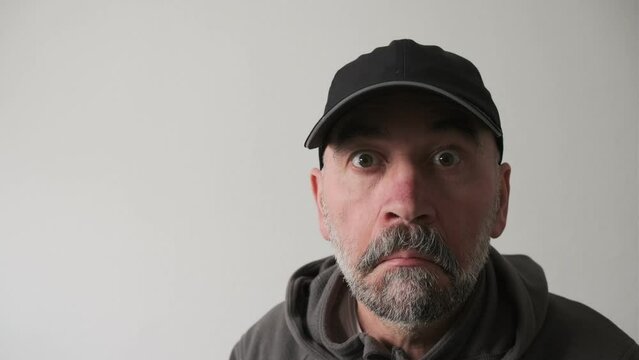 Close up portrait of serious old man with grey beard in the glasses looking astonishment to the camera.