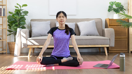 Beautiful healthy woman practicing yoga, Stretch or warm up before exercising, Calming the mind and meditating in her living room, Dumbbells and a protein shake or bottle of water, Healthy exercise.