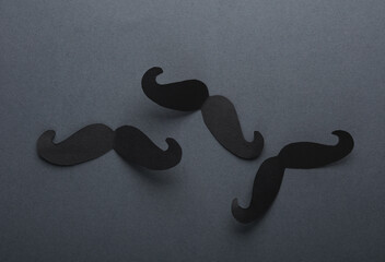 Lots of black paper mustaches on dark background. Father's Day. Top view. Flat lay