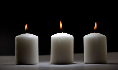 Obraz na płótnie Canvas three burning candles on white table with black background, space for text