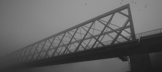 Silhouette of the bridge over river on a misty autumn day