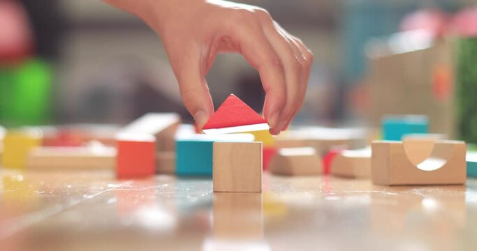 Close-up of girl's hand building house with wooden blocks