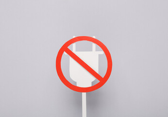 Paper electric plug with a prohibition sign on a gray background