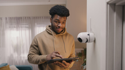 African American man installs security camera. Man sets up angle of CCTV camera at home and rotates...