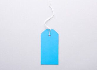 Blue blank clothing price tag or label mockup with string on gray background. Sale, shopping concept. Top view