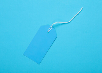 Blue blank clothing price tag or label mockup with string on blue background. Sale, shopping concept. Top view