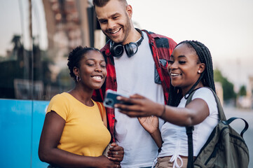 Obraz premium Multiracial friends taking selfie with a smartphone on a bus stop