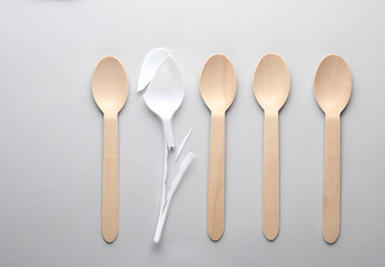 Broken plastic spoon and wooden spoons on a gray background. Plastic free, recycling, eco concept