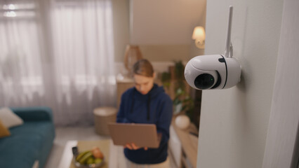 Caucasian woman installs security camera. Woman sets up angle of CCTV camera at home and rotates it...