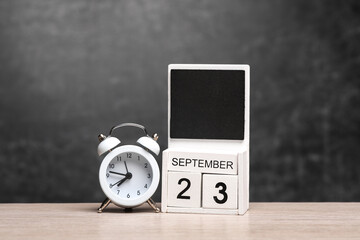 Calendar with september 23 date and alarm clock on table against chalk board background
