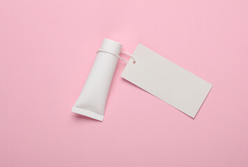 White cream tube with an empty price tag on a string, pink background. Beauty layout