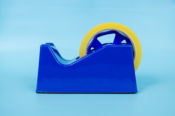 Blue tape dispenser with transparent tape isolated on blue background.