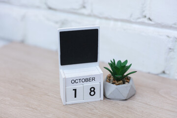 Wooden calendar with date October 18 and plant on table against brick wall background. Deadline, planning, business concept