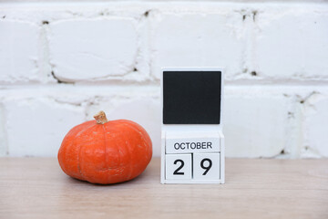 Wooden calendar with the date October 29 and pumpkin on a wooden table.