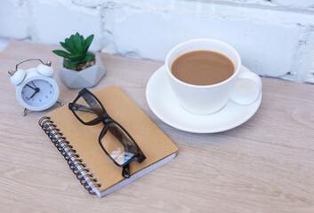 Coffee break. Coffee cup with notebook on table against background of white brick wall