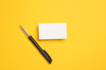 White business card with a pen on yellow background