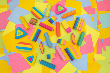 various shapes and colors of erasers arranged on a table with multicolored paper sticky notes on background